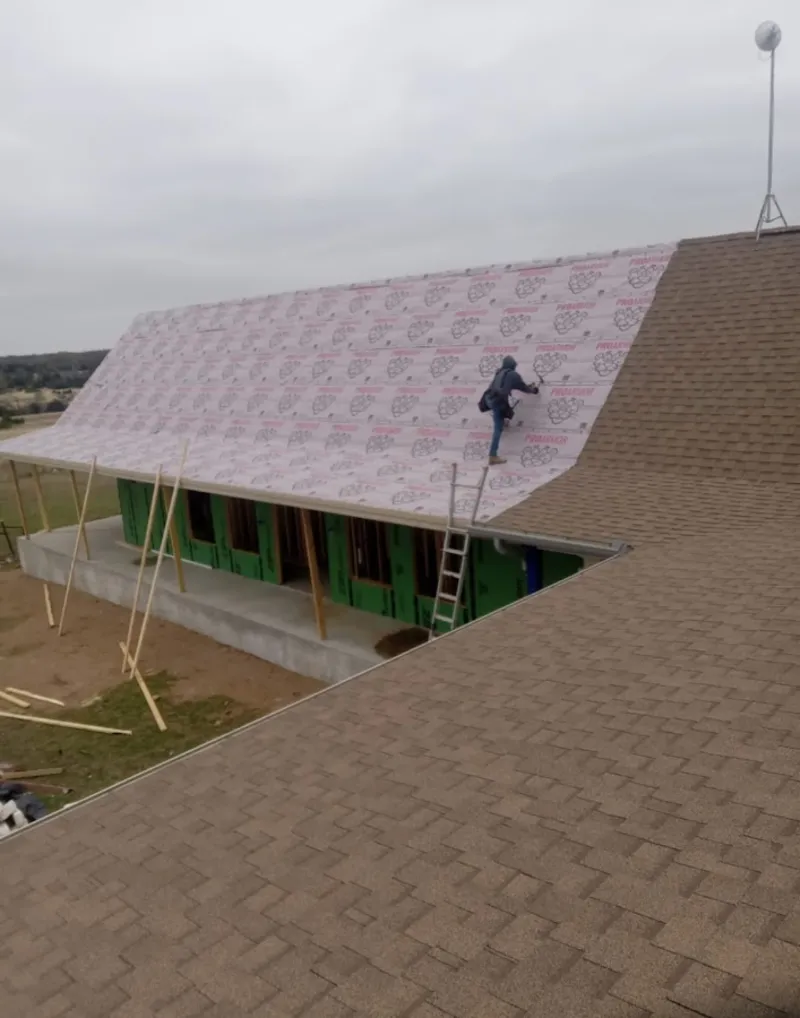 Worker preparing underlayment for a metal roof installation in Orono